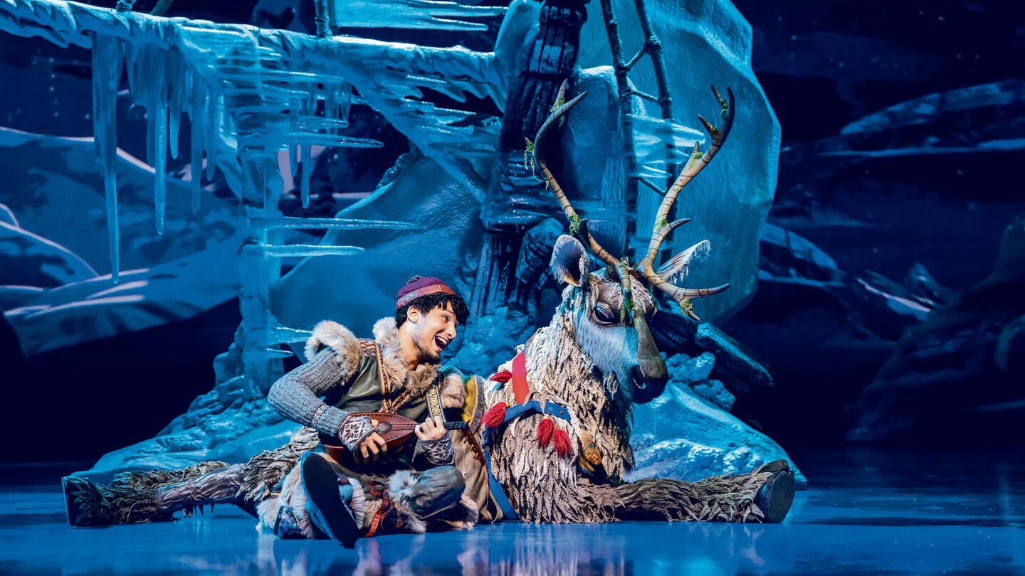 Ein junger Mann sitzt auf dem Boden neben seinem Rentier und spielt auf einer Ukulele.