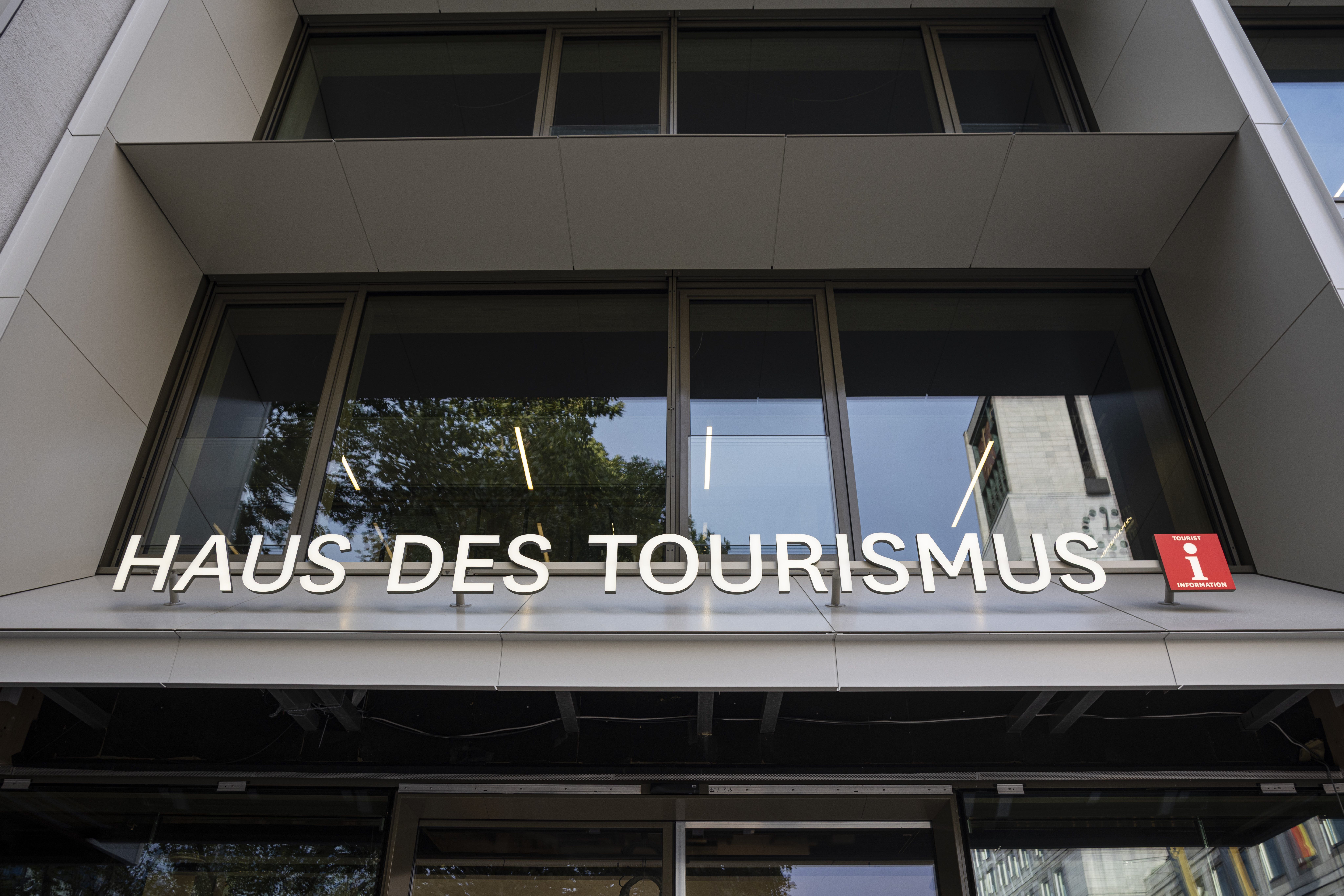 Weißer Schriftzug in Großbuchstaben über dem Eingang des i-Punkts. Dahinter das typische weiße "i" auf rotem Hintergrund, das die Tourist-Info symbolisiert.