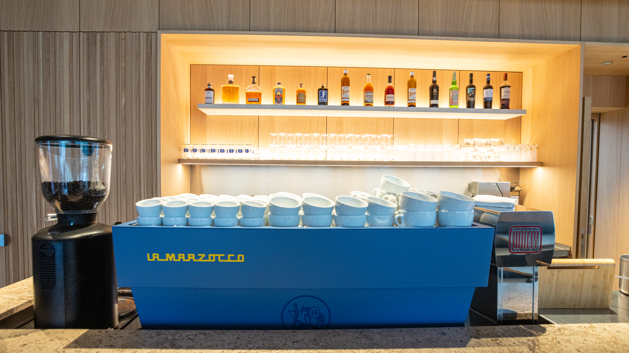 Große Siebträgermaschine und Kaffeemühle im Vordergrund, im Hintergrund Regal mit Gläsern und verschiedenen Spirituosen.