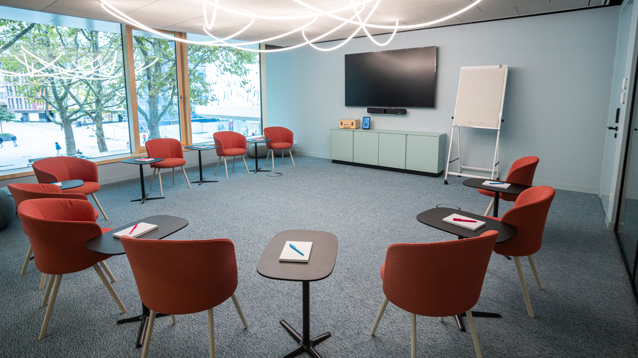 Raum Zukunft, Stuttgart-Marketing GmbH, Sarah Schmid Blick auf rote Stühle, die im Kreis angeordnet sind, auf das Display und das Flipchart.