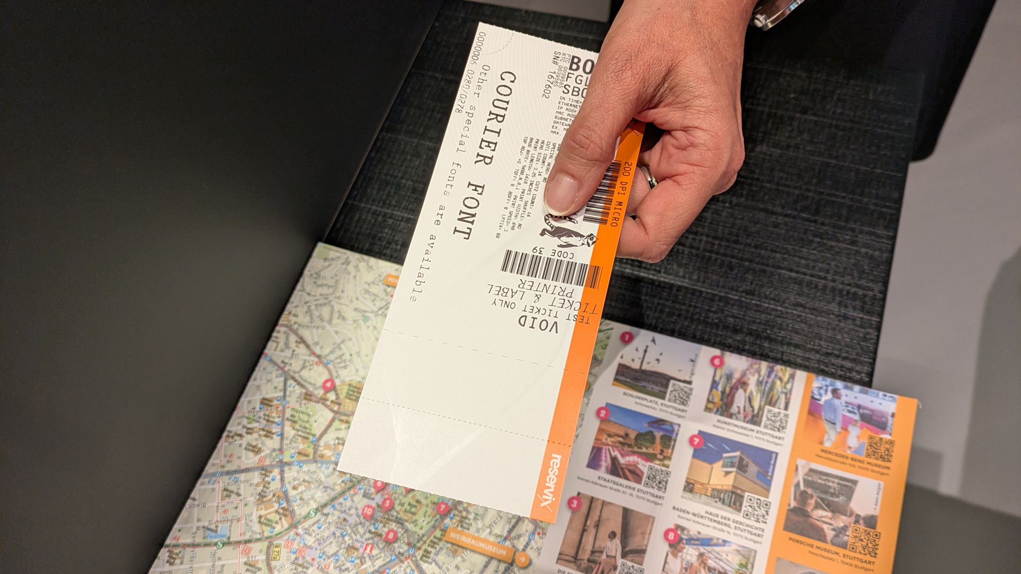 Die Person am Counter überreicht der betrachtenden Person ein Hardticket.