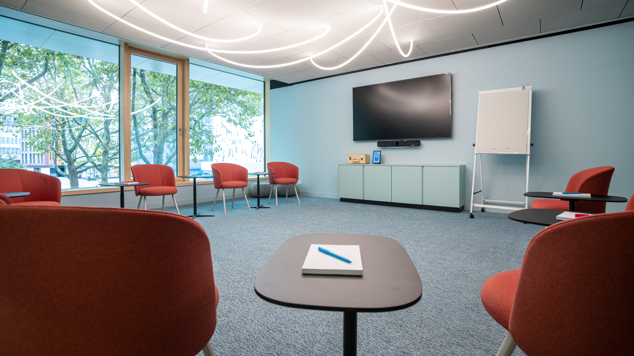 Raum Zukunft, Stuttgart-Marketing GmbH, Sarah Schmid Blick nach vorne, auf das 85“ UHD Display und das Flipchart. Auf der linken Seite Blick auf den Marktplatz. Rote Stühle stehen im Halbkreis.