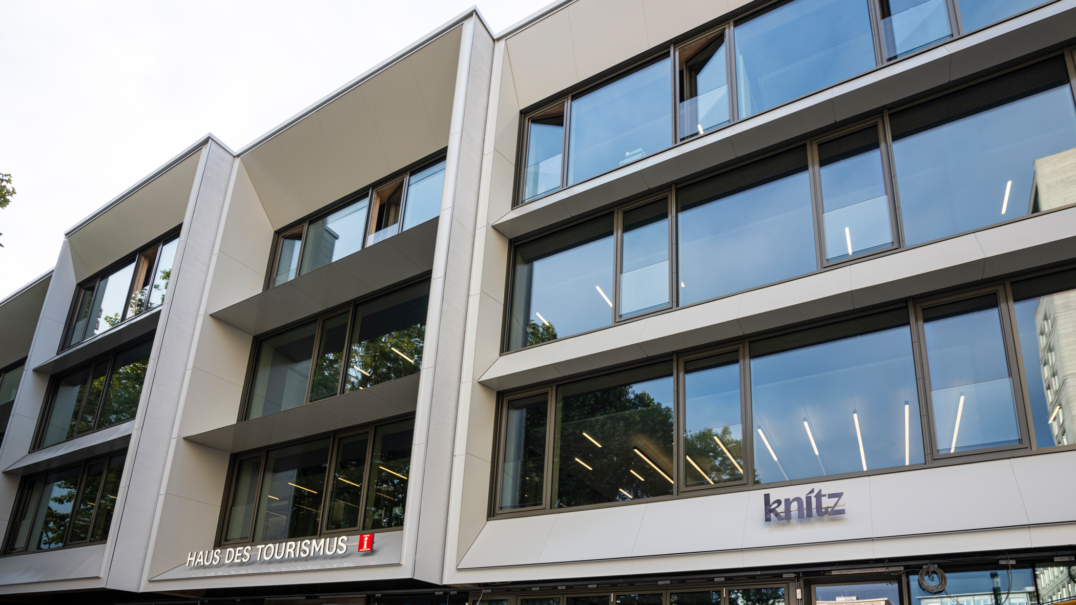 Blick am Gebäude hoch, unten im Bild die Schriftzüge über den Eingängen zur Tourist-Information und zur Gastro: Haus des Tourismus sowie knitz.