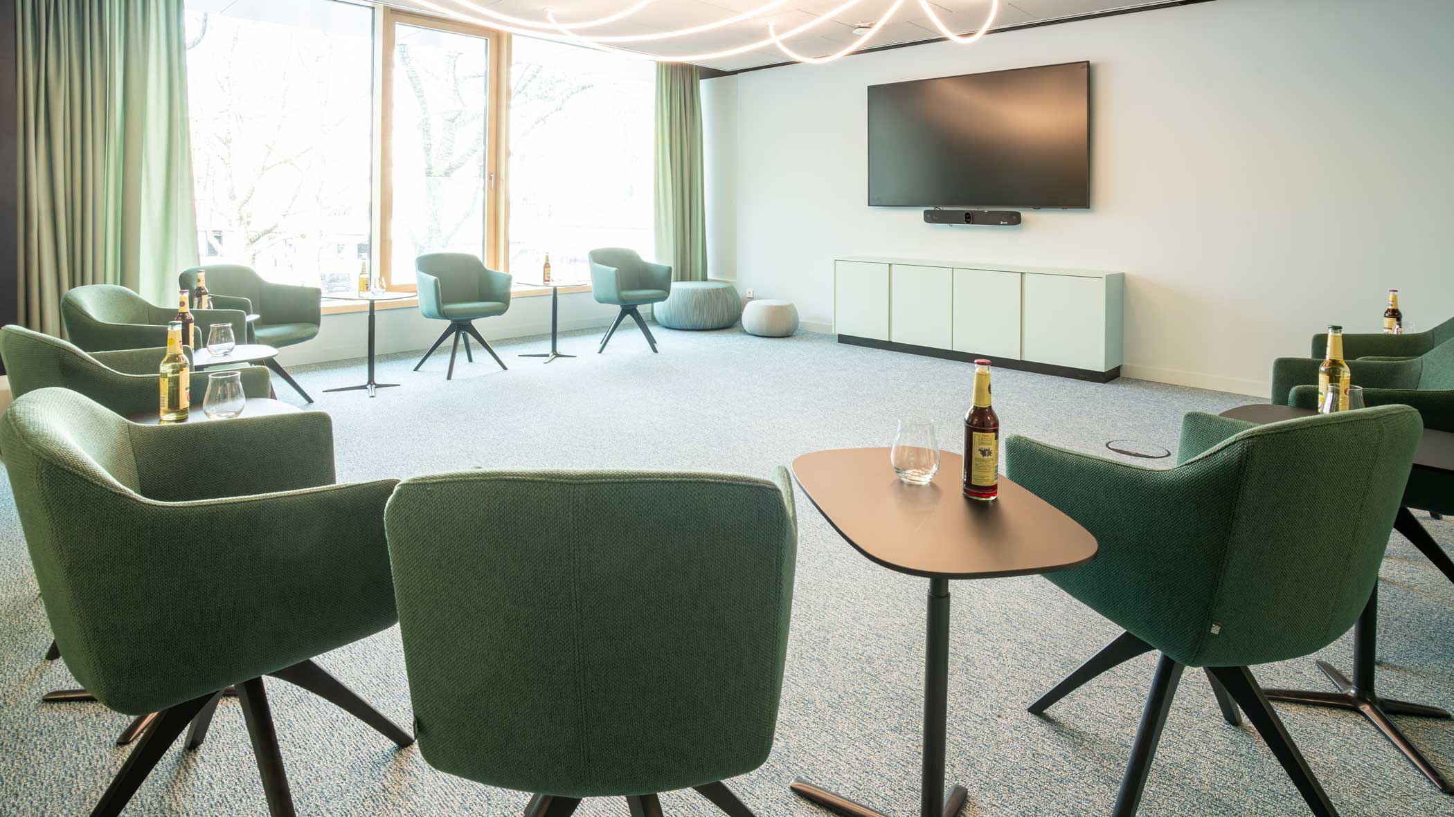 Grüne Stühle sind im Halbkreis angeordnet; an der Stirnseite des Raums ist ein flacher Bildschirm montiert, die großen Fenster blicken auf den Marktplatz.